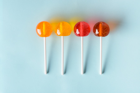 Different colored and flavoured big shiny lollipops on blue pastel background flatlay top view with long shadowsの写真素材