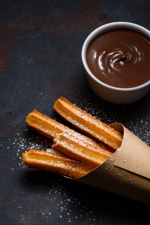 Churros in paper bag with sugar and chocolate sauce on dark black backgroundの写真素材