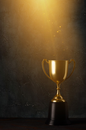 Golden trophy cup on dark table with rays of light and glitter dust dark backgroundの写真素材