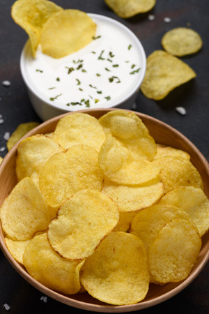 Potato chips in bowl with sauce dip on dark tableの写真素材