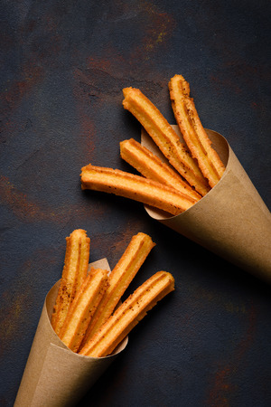 Churros sticks fresh hot with cinnamon in paper bag on dark background top viewの写真素材