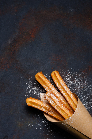 Churros sticks fresh hot in paper bag on dark background top view with copy spaceの写真素材