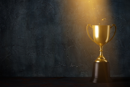 Golden trophy cup on dark table with rays of light and glitter dust dark background with copy spaceの写真素材