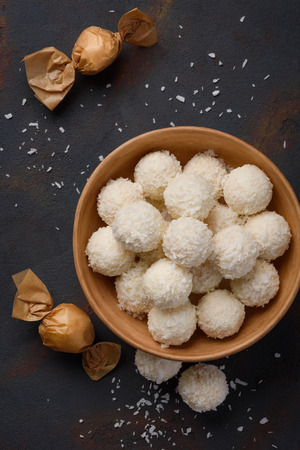Coconut candies in bowl and wrapped in paper on dark table background flat lay top viewの写真素材