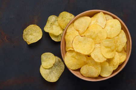 Crispy potato chips in bowl on dark tableの写真素材