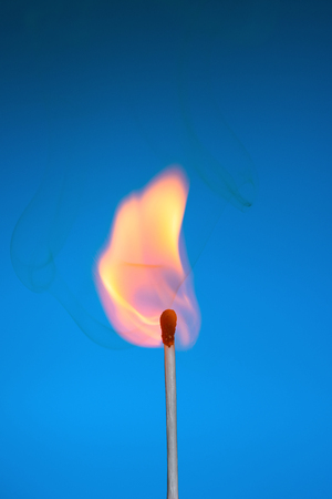 Burning match stickwith fire and smoke on blue backgroundの写真素材
