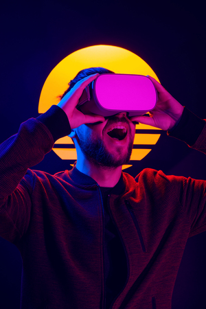 Man wearing virtual reality goggles experiencing fun entertainment. VR head set videogame in 80's synthwave and retrowave futuristic aesthetics.の写真素材