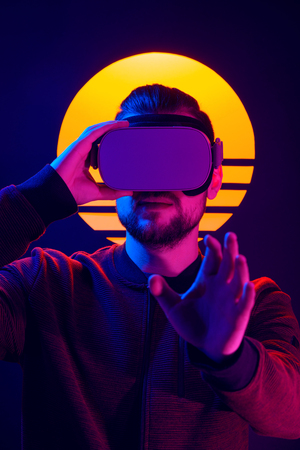 VR videogame experience in 80's synthwave and retrowave futuristic aesthetics. Man wearing virtual reality goggles wireless headset and interacting with hand gestures.の写真素材