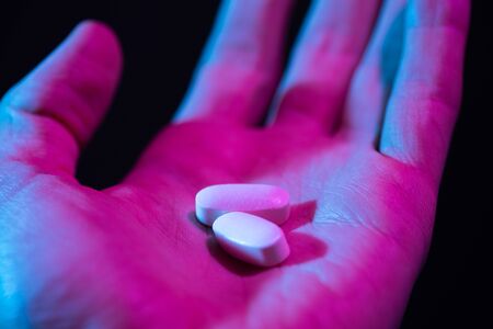 Pills in hand. Two drug tablets in palm close-up on dark backgroundの写真素材