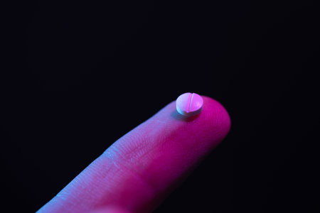 Pill on fingertip. Small white drug tablet on the tip of a finger.