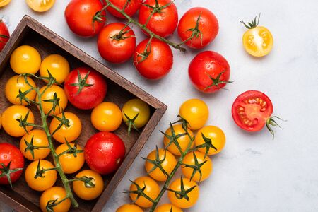 Tomatoes variety on rustic table in wooden box red yellow whole and cut, top view