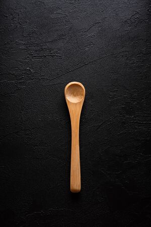 Empty new clean small bamboo wooden spoon on black dark table background top view flat lay.の写真素材