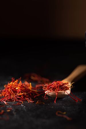 Saffron spices heap and wooden spoon on black slate stone table. Saffron flavor and coloring seasoning ingredient.の写真素材