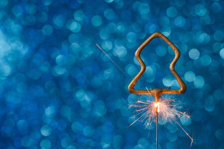 Burning sparkler in christmas tree shape on blue glitter background with copy-space.の写真素材