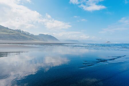 Ocean beach with blue sky reflection on wet sandの写真素材