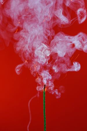 Burning fuse wick with sparks and smoke on red backgroundの写真素材