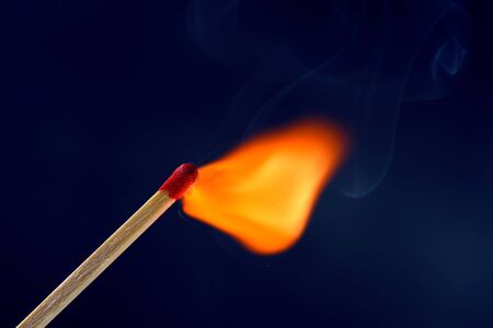 Match stick ignited burning bright big fire flame with blue smoke on dark background.の写真素材