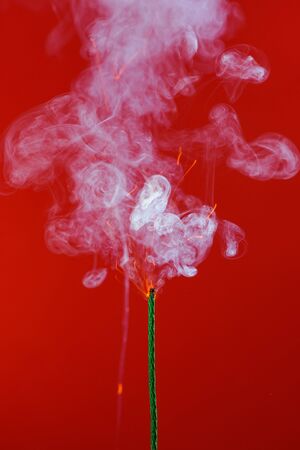 Burning fuse wick with sparks and smoke on red backgroundの写真素材