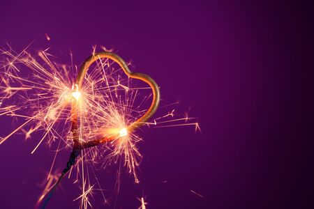 Sparkler in love heart shape on a purple background with lots of sparks. Wedding or Valentine's day celebration banner with copy-space..の写真素材