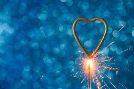 Burning sparkler in heart love shape over blue festive glitter background. Wedding or valentine's day banner with copy-space.の写真素材