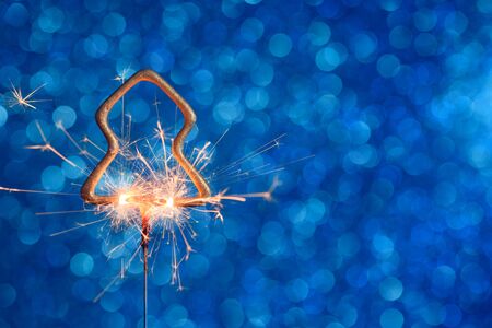 Burning golden sparkler in christmas tree shape on blue glitter background with copy-space.の写真素材