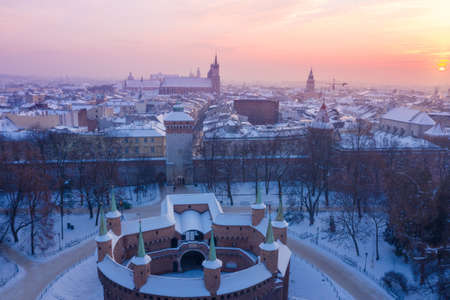 Barbikan and Krakow Old Town in winter. Snow on roofs in winter Krakow Poland at sunset. Medieval Barbacan fortification, Royal Road and city center.の写真素材