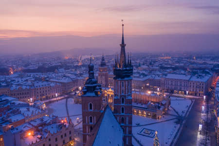 Main square Rynek of the Old Town of Krakow Poland in winter. St. Mary's Basilica Gothic church, Town Hall Tower, Krakow Cloth Hall, covered in snow at twilight with Christmas tree, decorations and lights.の写真素材