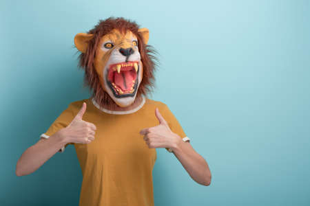 Young woman in lion mask keeps thumb up approval gesture, isolated on blue background.の写真素材