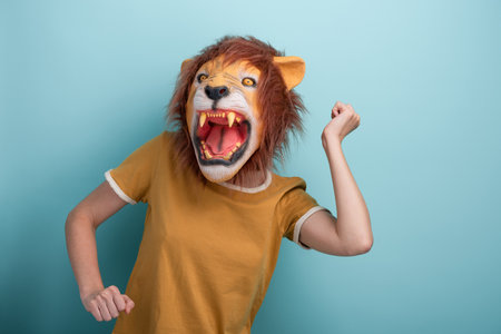Young woman in lion mask perform carefree dance moves, isolated on blue background.の写真素材