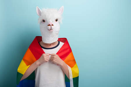 Young woman in lion mask proudly hold rainbow lgbt pride flag wrapped around the shoulders, isolated on blue background with copy-space.の写真素材