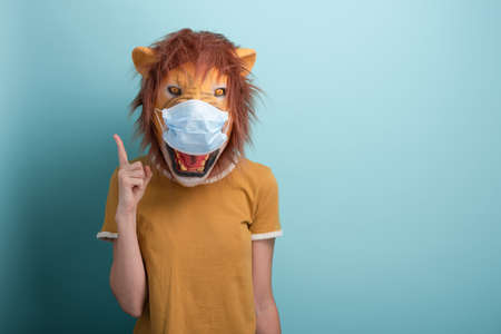 Young woman wearing lion and protection medical mask pointing up with index finger, capture the attention or warning advice, isolated on blue background.の写真素材
