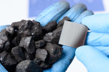Handful of coal in one hand and solar panel in other. Transition from fossil fuel to clean energy research concept.の写真素材