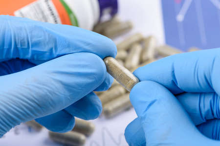 Transparent supplement capsule in scientist hands, bottle and pills on background.の写真素材