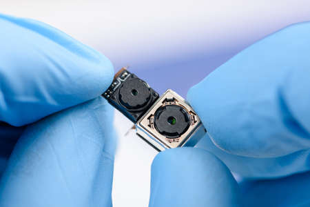 Two cell phone camera modules in scientist hands.の写真素材