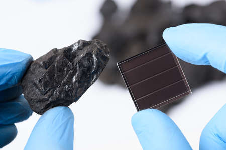 Coal next to solar panel in scientist hands in laboratory. Fossil fuel to green renewable energy transition concept.の写真素材