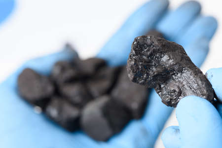 Coal lump in scientist hand and small heap in other. Fossil fuel energy research concept.の写真素材