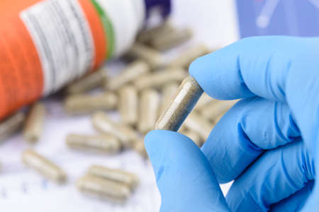Supplement capsule in scientist hands, with bottle and pills on background.の写真素材