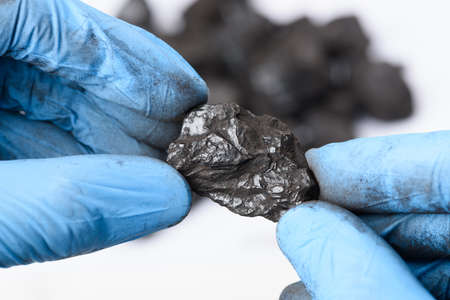 Hands in gloves hold lump of black coal in laboratory. Fossil fuel research concept.の写真素材