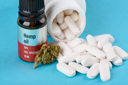 Full spectrum hemo oil with CBD cannabis flower bud and bottle with white medical pills on blue backgroundの写真素材