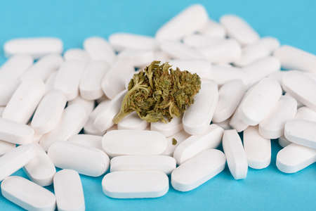 CBD cannabis flower bud on heap of white medical pills on blue backgroundの写真素材
