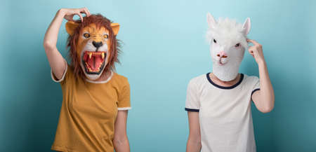 Young woman in lion and alpaca mask thinking, scratching her head, isolated on blue backgroundの写真素材