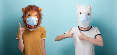 Young woman wearing lion and protection medical mask pointing up with index finger, and in alpaca mask keeps thumb up approval gestureの写真素材