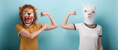 Young woman in lion and alpaca mask flexing arm muscles, isolated on blue background with copy-space.の写真素材