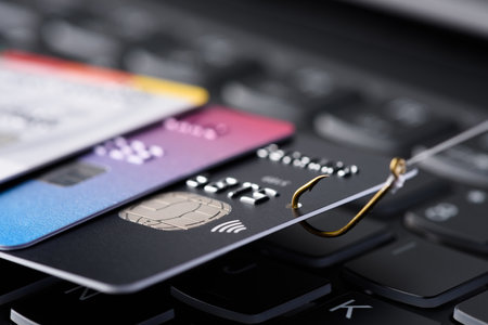 Credit card phishing scam concept. Credit card data theft, card hooked on fishing hook pulled from stack of other cards on keyboard.の写真素材
