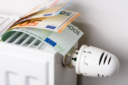 Euro money banknotes in heating radiator battery with thermostat temperature regulator. Concept of expensive heating costs and rising energy bill prices for winter cold season.の写真素材