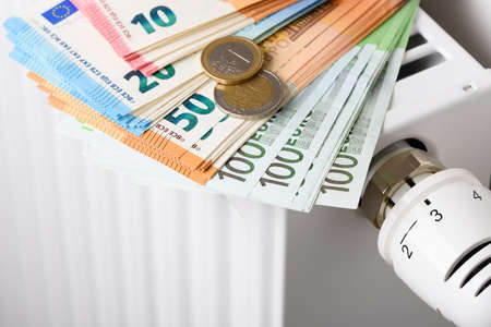 Room heating radiator battery with thermostat temperature regulator and euro money banknotes on it. Concept of expensive heating costs and rising gas and electricity energy bill prices for winter cold season.の写真素材
