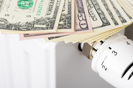 Stack of dollar banknotes on heating radiator battery with thermostat temperature regulator. Concept...