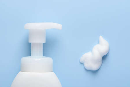 White cosmetic bottle with pump dispenser and foam smear on blue background top view flat layの写真素材