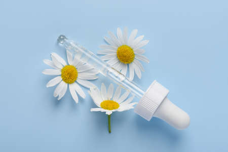 Skincare serum dropper with chamomile flowers on blue background top viewの写真素材