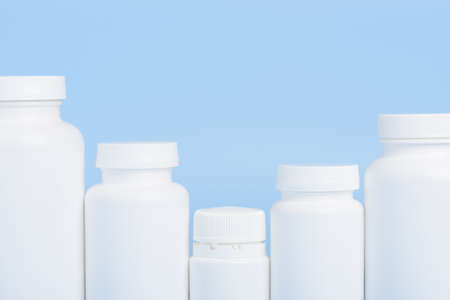 Row of blank white plastic bottles of medicine pills or supplements on blue backgroundの写真素材